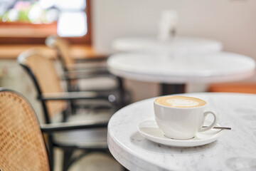 A cup of hot cappuccino on the table in the coworking space of the coffee shop. A cup of coffee on the veranda on a sunny day. Coffee break at the cafe. Close-up