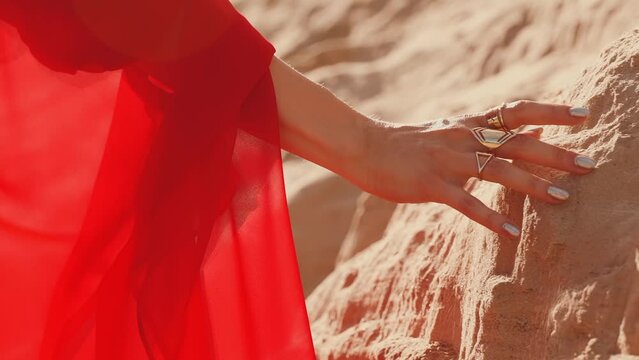 closeup arabic style female hand stroking touching yellow sand dune desert. body part arm Girl wearing fingers golden rings set luxury jewels. Traditional Arab Hijab Silk Red Dress Back rear view