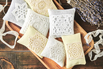 Sachet bags decorated with crocheted lace and lavender on a wooden background