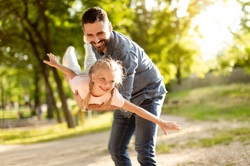 Carefree summer moment. Excited father holding his cute daughter on hands, playful girl enjoying...