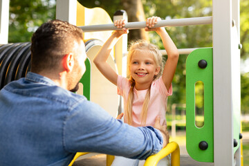 Tales from the playground. Father playing with his little happy daughter in the park, girl sitting...