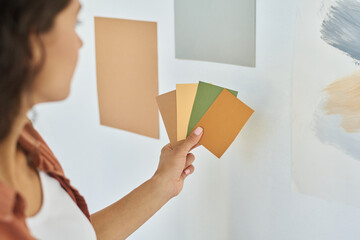 Hand of young woman with palette of color swatches choosing one for walls of living room or bedroom...