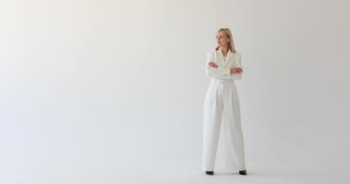 Confident and businesslike woman dressed in formal attire, standing against a pristine white backdrop. She glances thoughtfully to the side, projecting an air of contemplation and determination.