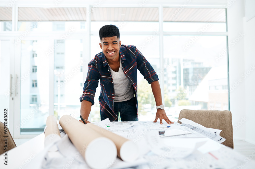 Wall mural At the head of the design helm. Portrait of a young man going over blueprints in a modern office.