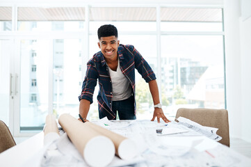 At the head of the design helm. Portrait of a young man going over blueprints in a modern office.