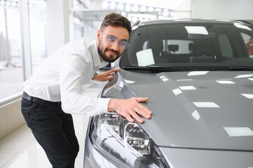 Happy young guy checking new luxury car, buying automobile at dealership centre. Portrait of...