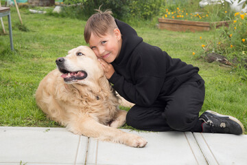 A boy with a dog, a Golden Retriever on the grass near the house.