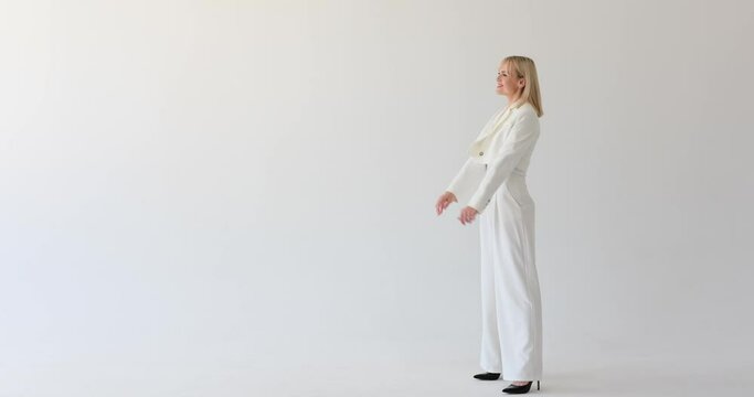 A cheerful woman is seen on a white backdrop, dressed in a white suit, and looking to her left with a bright and friendly smile. Her positive expression create a sense of warmth and approachability.