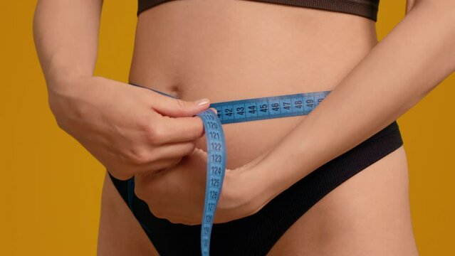 Close up woman with measurement tape around her pregnant body counting centimeters over orange screen background. Healthy pregnant female keeping track of the belly circumference.