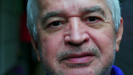 Close-up face of a mature unshaven senior man with gray hair and wrinkles staring at camera in macro portrait displaying old age experience
