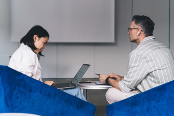 Focused diverse colleagues working on laptop in office classroom