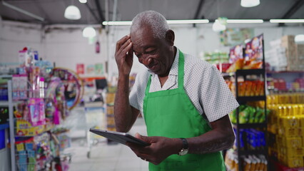 Confused senior worker of supermarket using technology feeling frustration, scratching forehead while holding tablet device