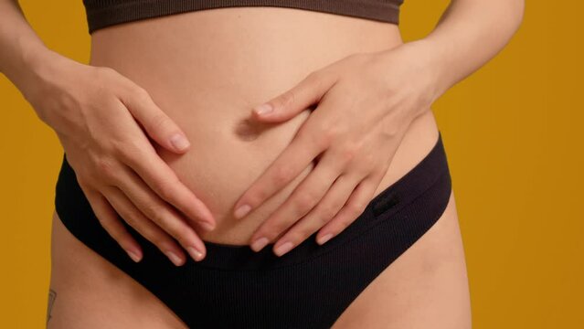 Pregnant woman in black panties touching her belly on orange screen background. Family awaiting a new member.