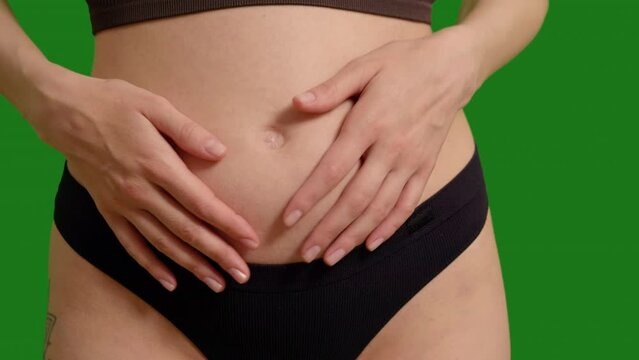 Pregnant woman in black panties touching her belly on green screen background. Family awaiting a new member.