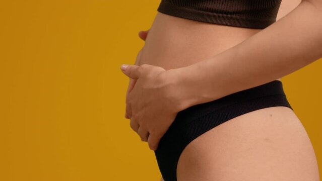 Front and side view of early pregnant woman obsessed with her growing stomach on orange screen background. Healthcare during pregnancy, female making energetic connection with her fetus.