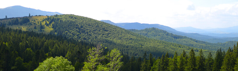 Range of mountains covered in green trees. The sky is blue with a few clouds.