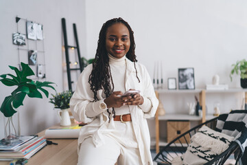 Cheerful black woman with smartphone in workplace
