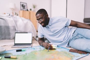 Black man with map and laptop in apartment