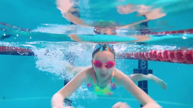 Child girl or teenager swims underwater in the pool. Shooting a video underwater as a child swims in a pool