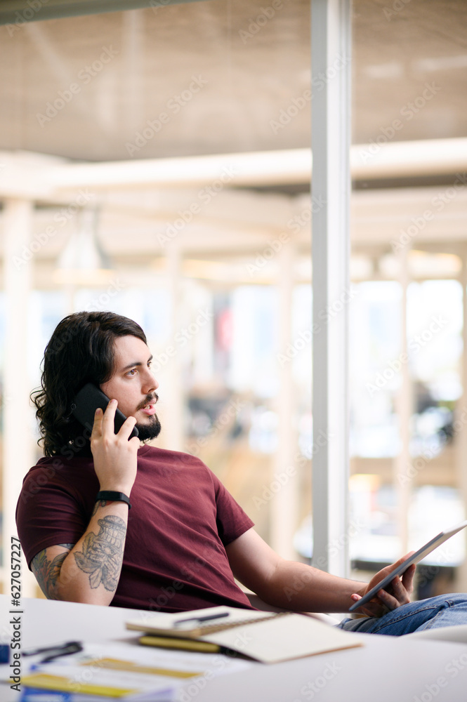 Poster do you have any news for me. shot of a young businessman talking on a cellphone while using a digita