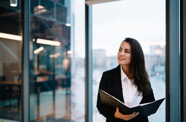 Positive businesswoman with folder standing in modern workspace