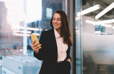 Cheerful businesswoman browsing cellphone during workday in office