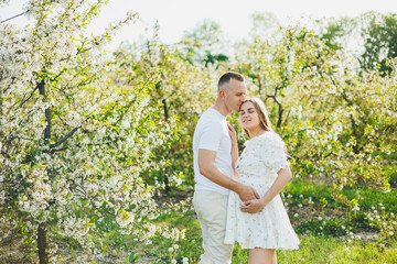 The concept of happy family relationships. A young happy couple in anticipation of pregnancy walks through a blooming garden. Couple in love in blossoming apple trees.