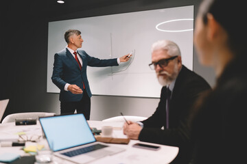 Elderly businessman drawing chart on whiteboard during meeting