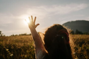 Silhouette of preteen girl raising hand over sunset sky, enjoying life and nature. Child on summer...