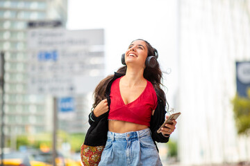 Fototapeta premium happy young woman walking in city with phone and headphones