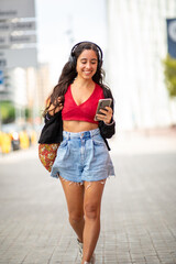 young woman walking in city with mobile phone and headphones