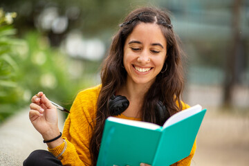 Fototapeta premium happy young woman sitting with book and pen