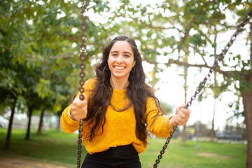 smiling young woman swinging in the park - obrazy, fototapety, plakaty