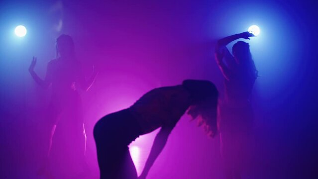 Sexy dance of a group of women in the rays of colored light. Enchanting movements of female bodies in a dance in a smoky room. High quality 4k footage