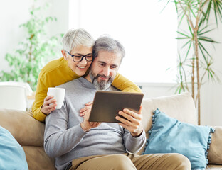 woman couple senior man happy internet love tablet together mature active elderly retirement computer technology online using caucasian home adult family romance - obrazy, fototapety, plakaty