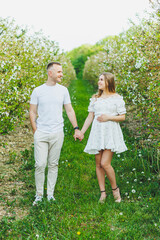 Beautiful young couple man and pregnant woman in spring garden. Beauty lifestyle family concept. A happy mother is expecting a baby. A happy young couple in a blooming garden