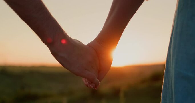 A young couple holds hands against the backdrop of a picturesque valley where the sun sets