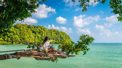 Traveler woman relaxing on tree branch using tablet at Railay beach Krabi, Asia business people on vacation at resort work with computer notebook, Tourist travel Phuket Thailand summer holiday trip