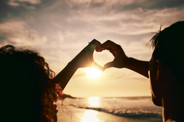 People with heart hands, sunset on beach, silhouette with love and romance sign, travel and...
