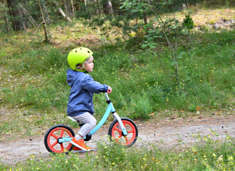 Little boy riding his balance bike in the forest.
