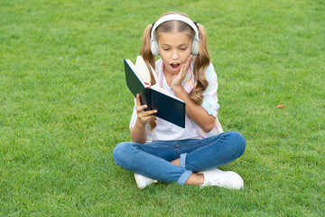 Naklejka na ściany i meble music education while listening. lifestyle of teenager girl outdoor. surprised and curious teen girl. education through self reading book. audio book or ebook. teen girl lifestyle. relax in park