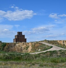 The road climbs to the top of the hill, where there is a three-story frame made of coniferous wood on a summer day