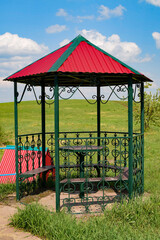 A new metal gazebo with a table and benches on the background of a blooming apple tree and a green meadow on a spring day
