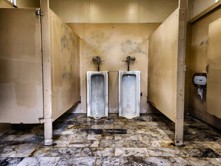 semi abandoned men's public toilet, very dirty and ruined, yellow light, dirty marble floor with...