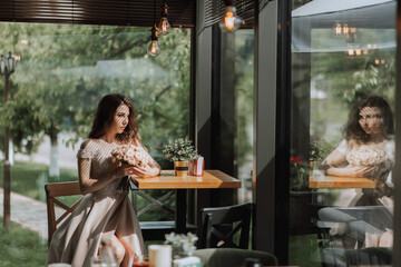 A young stylish woman in a beige dress with a bouquet of flowers in her hands is sitting in a beautiful light in a cafe in Spain
