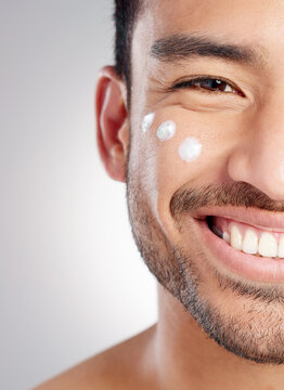 Closeup, portrait and man with skincare, cream and dermatology against grey studio background. Face, male person and model with lotion, creme and grooming routine with a smile, beauty and smooth skin
