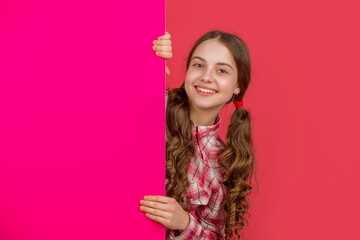 positive teen kid behind blank pink paper with copy space for advertisement