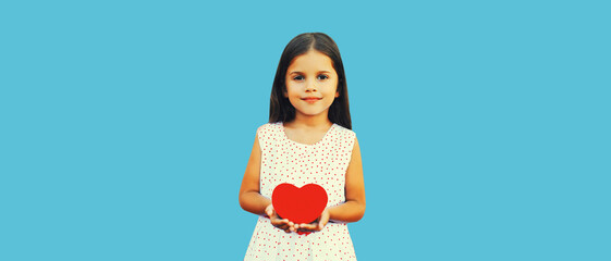 Portrait of happy child girl holding red paper heart on blue background