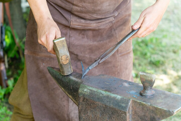 A blacksmith in a brown leather apron is forging a piece of iron on an anvil