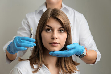 Portrait of a young girl and hands of a beautician with a syringe, cosmetic injections.